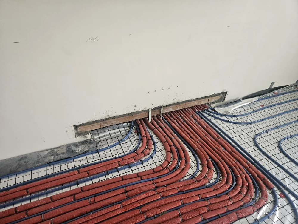 Instalacje hydrauliczne – rozłożone na stelażu czerwone i niebieskie rury ogrzewania podłogowego