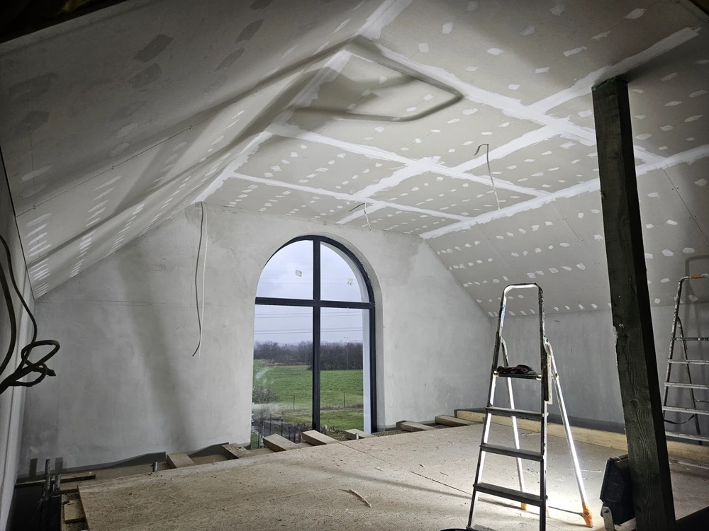 Zabudowa poddasza z montażem płyt g-k na skośnym suficie, stelaż i drabina na pierwszym planie