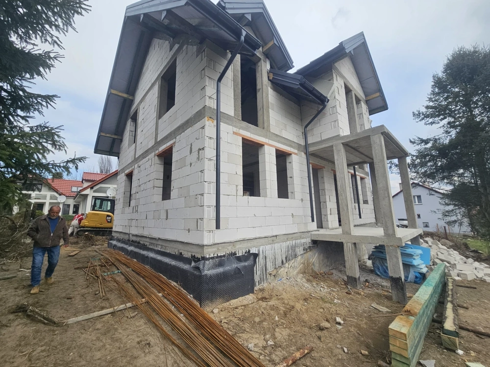 Dom jednorodzinny w stanie surowym otwartym z widoczną konstrukcją ścian z bloczków i zadaszeniem