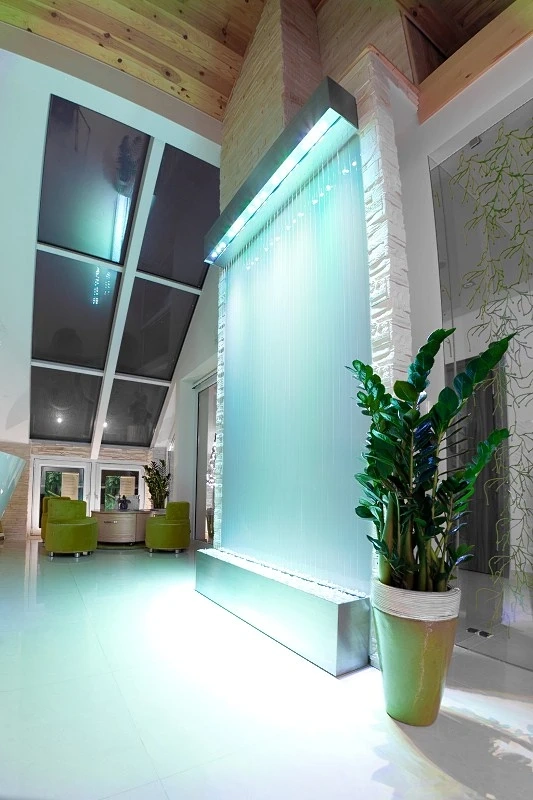 Nowoczesna wewnętrzna ściana wodna z podświetleniem i zielonymi fotelami – wykończenia wnętrz