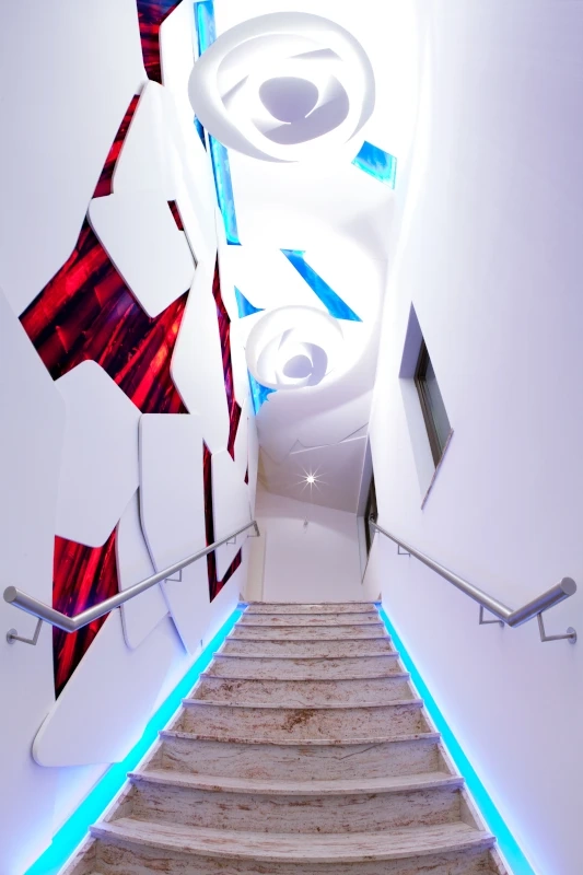 Nowoczesne wykończenie wnętrz: białe schody z podświetleniem LED i abstrakcyjną dekoracją ściany