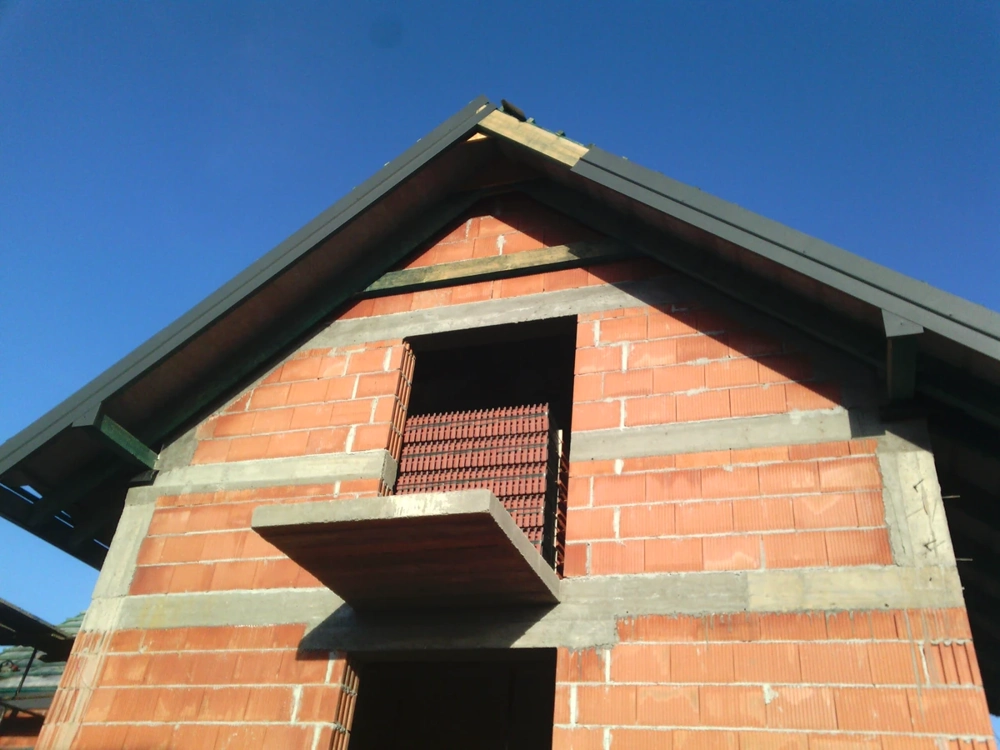 Elewacja domu jednorodzinnego w stanie surowym otwartym (Stan surowy otwarty) z czerwonych pustaków i widoczną konstrukcją dachu