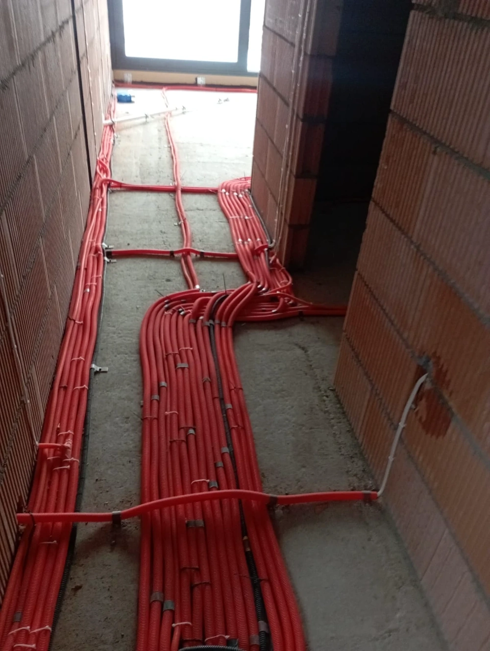Rozprowadzenie czerwonych rur instalacji elektrycznych w wylewce między murowanymi ścianami
