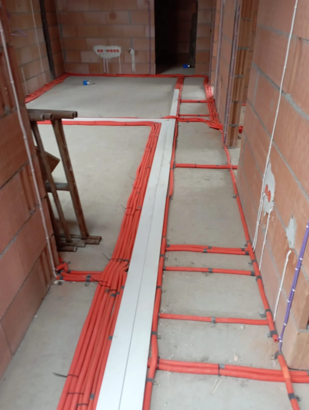 Widoczne instalacje elektryczne w korytkach podłogowych na surowym etapie budowy