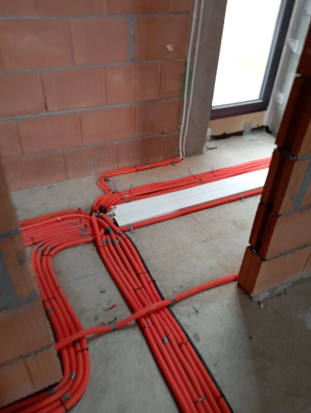 Czerwone peszle ułożone na betonowej posadzce, instalacje elektryczne w stanie surowym budynku