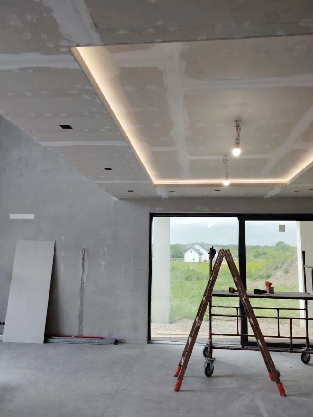 Wnętrze domu w stanie deweloperskim z sufitami podwieszanymi, płytami karton-gips i wstępnym tynkowaniem