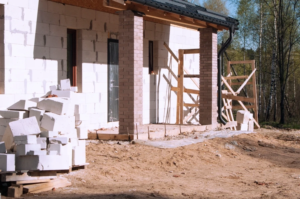 Dom w stanie surowym otwartym z murowanymi bloczkami, ceglanymi filarami i rusztowaniem przy elewacji