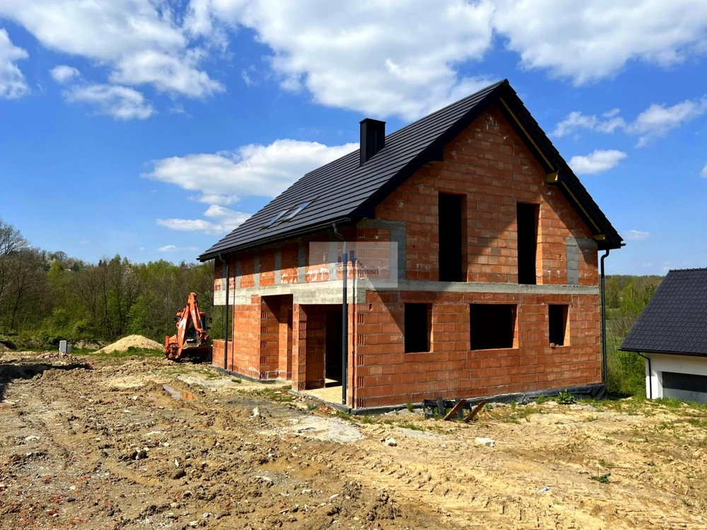 Dwukondygnacyjny dom jednorodzinny stan surowy zamknięty na placu budowy z koparką