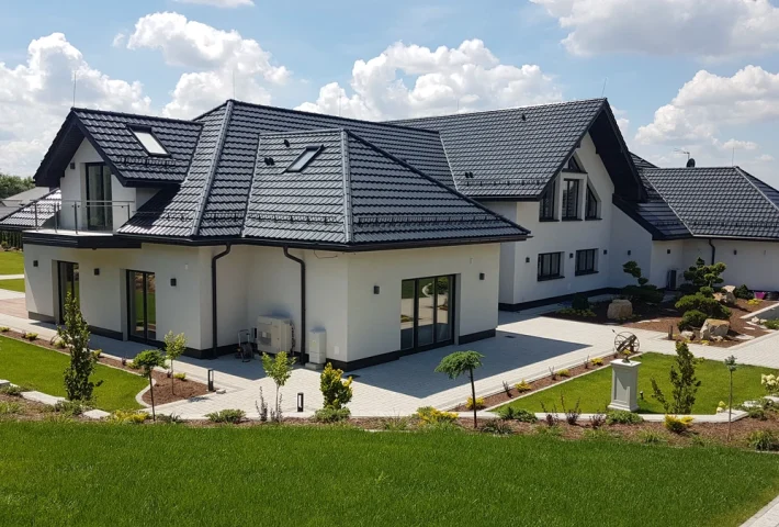 Nowoczesny dom jednorodzinny z białą elewacją i ciemnym dachem oraz zadbanym otoczeniem Domy jednorodzinne