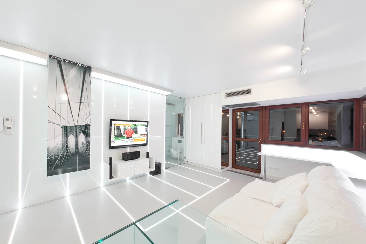 Wykończenia wnętrz w salonie z białą zabudową, zintegrowanym oświetleniem LED, szklaną ścianką i telewizorem